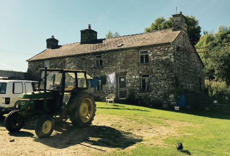 Photo of stone farmhouse with tractor and truck in front